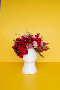 Close-up of red roses in vase against yellow background