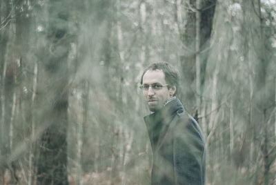 Portrait of man standing amidst trees at forest