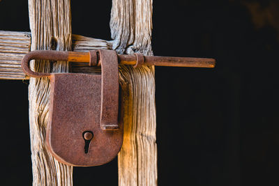 Close-up of rusty padlock on door against black background