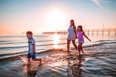 Mother with children walking in sea on shore at beach during sunset