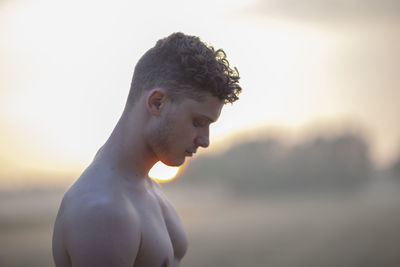 Side view of shirtless young man against sky