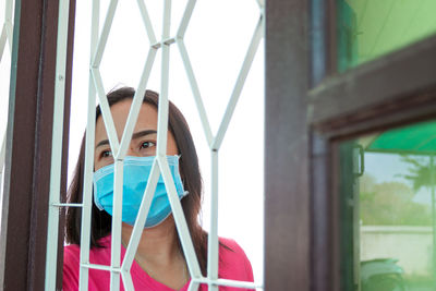 Low angel view of mature woman wearing flu mask standing by window