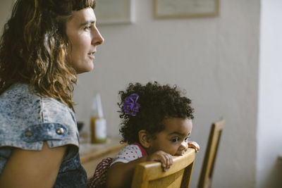 Side view of mother sitting by daughter biting chair at home