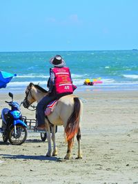 Full length of man riding motorcycle on beach against clear sky