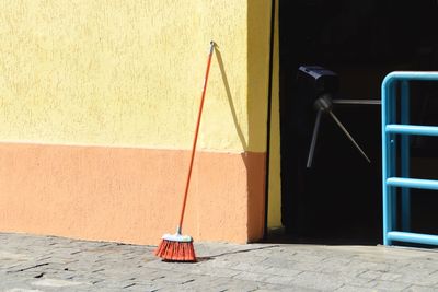 Broom on footpath against wall