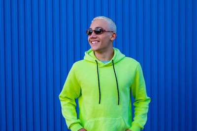 Man wearing sunglasses standing against blue wall