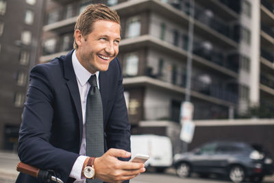 Happy businessman using smart phone in city