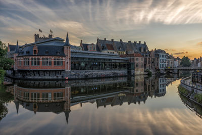 Buildings reflecting on canal in city during sunset