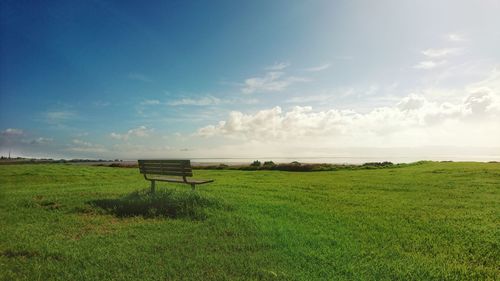 Empty bench on field against sky