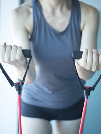 Midsection of woman stretching resistance band in gym