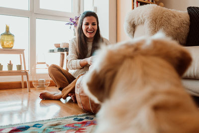 Happy woman looking at dog while sitting on floor