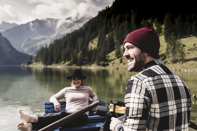 Young man sitting on lake against mountains