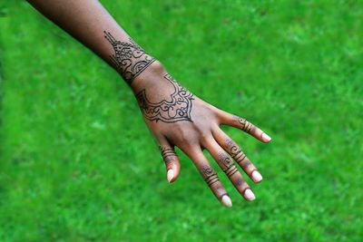Close-up of cropped hand with henna tattoo over grassy field
