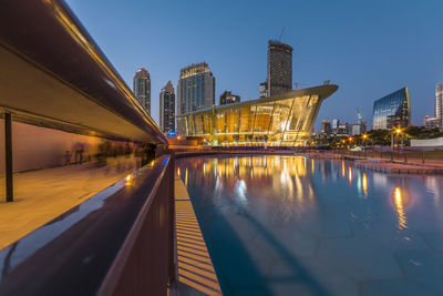 Illuminated buildings by river against sky at night