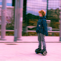 Full length of boy riding hoverboard on footpath in city