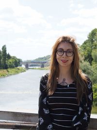 Portrait of young woman standing on bridge over river against sky