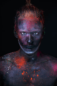 Close-up portrait of shirtless man with face paint against black background