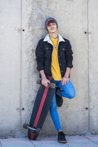 Full length of man with skateboard standing against wall