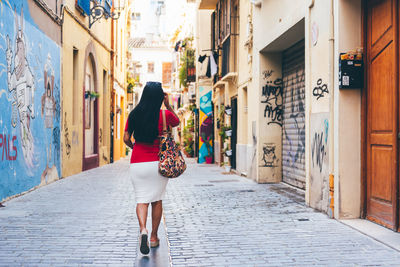 Woman walking on footpath amidst buildings in city