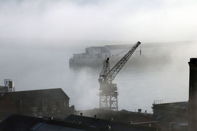 Cranes on pier by sea against sky