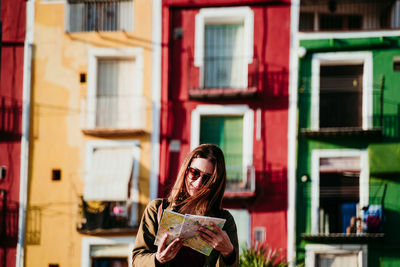 Smiling woman wearing sunglasses standing against buildings