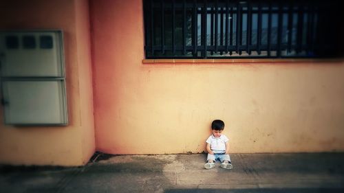 Cute boy sitting on sidewalk against house