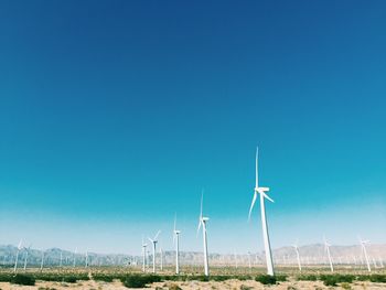 Windmills on field against clear blue sky