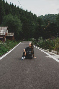 Woman sitting on road by trees