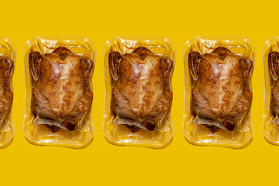 Vacuum packed roasted chickens arranged in a line on yellow background