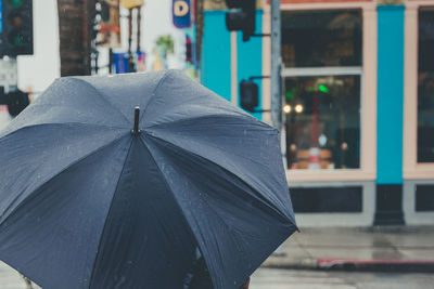 Close up of water hitting a plain black umbrella in the middle of a busy street.