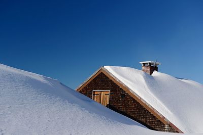 Low angle view of snow covered building against clear blue sky