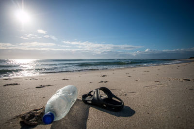 Close-up of bottle and flip-flop on beach against blue sky