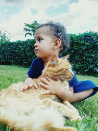 Boy stroking cat while sitting on grass in park