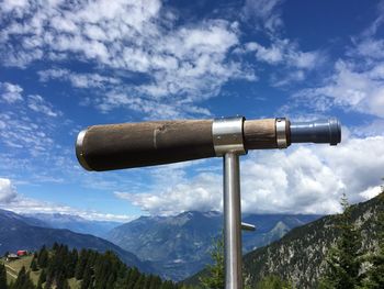 Low angle view of coin-operated binoculars by mountains against sky