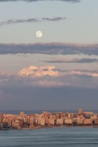 Sea by buildings against sky at dusk