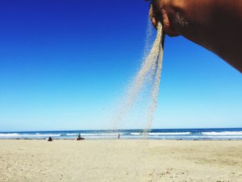 Man holding umbrella on beach against clear blue sky