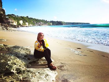 Portrait of young woman sitting on rock formation at dreamland beach