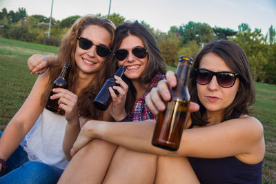 Portrait of young women drinking alcohol while sitting on field