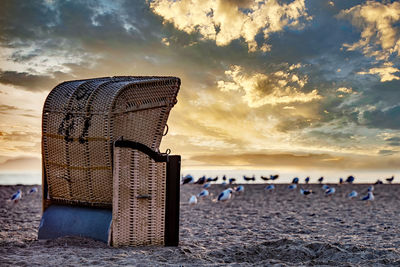 Hooded chairs on beach against sky during sunset