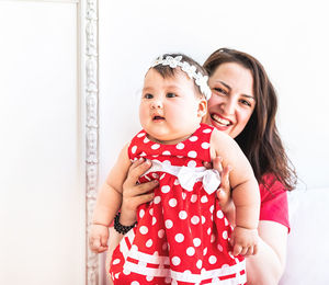 Portrait of mother and daughter standing against wall