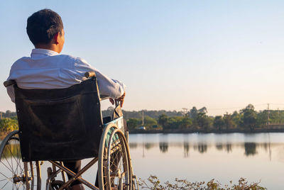 Rear view of man sitting by lake against sky