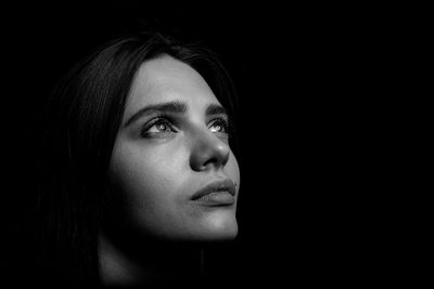 Close-up of young woman looking away against black background