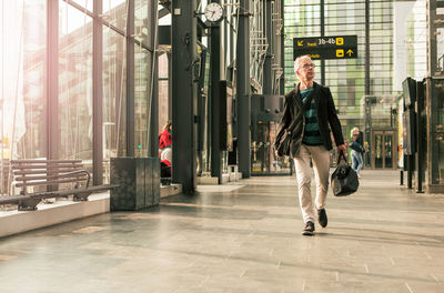 Full length of senior male commuter walking with luggage at railroad station