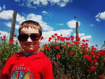 Portrait of smiling boy standing by poppies against sky