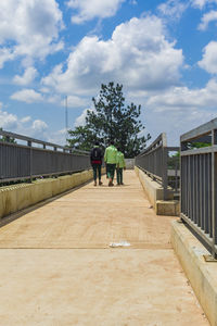 Rear view of men walking on footbridge against sky
