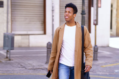 Young man looking away while walking on street in city