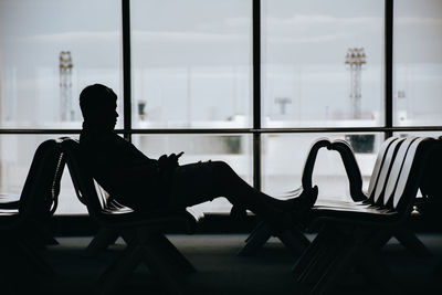 Silhouette man sitting on chair by window at airport