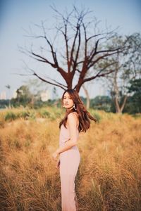 Portrait of young woman standing on grassy land against bare tree