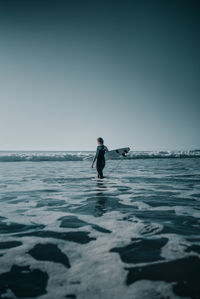 Woman carrying surfboard in sea against clear sky