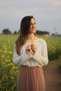 Beautiful woman holding flowers while standing on field